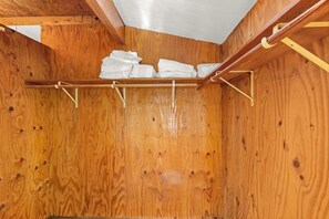 A wooden room with a ceiling and a shelf holding folded towels.