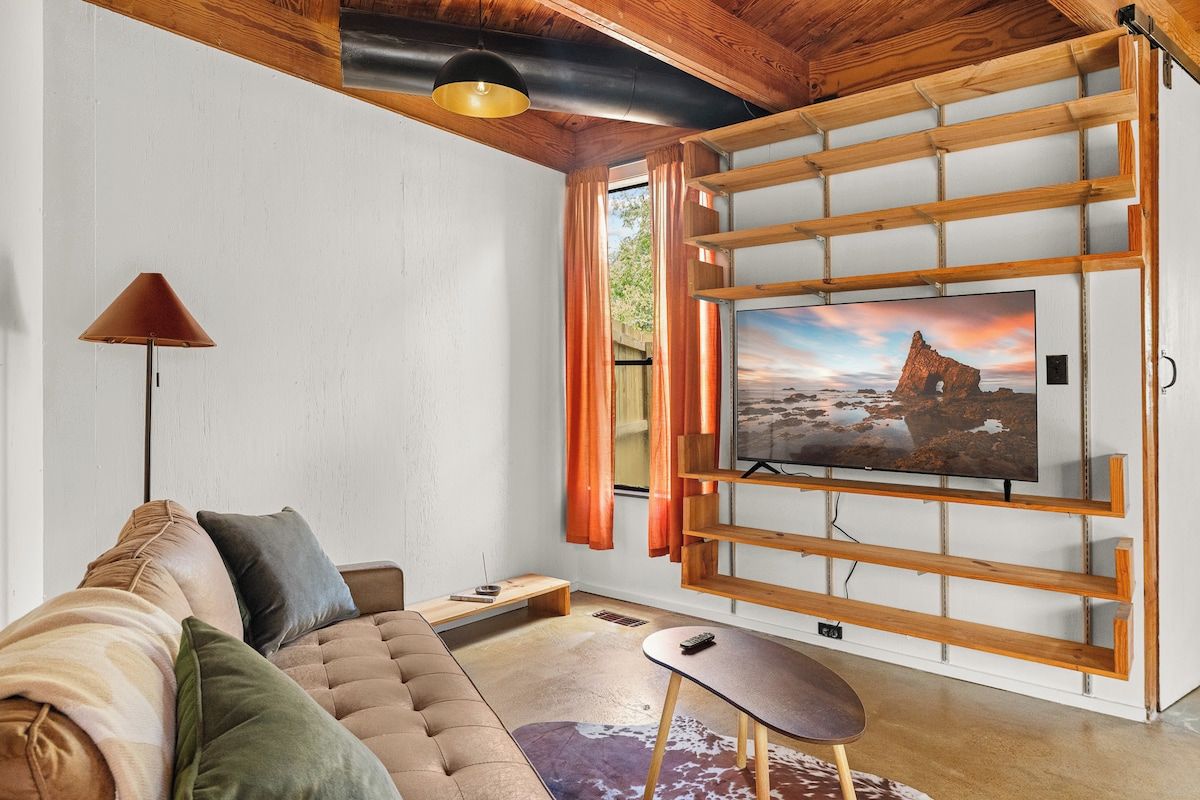 Un salon moderne avec un grand téléviseur à écran plat fixé à un mur en bois, un canapé avec des coussins, une petite table et une lampe.