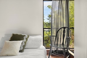 A bedroom with a bed, pillows, a chair, and a window with curtains.