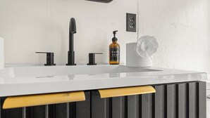 Une salle de bain avec un lavabo blanc, un robinet noir et un flacon de savon pour les mains.