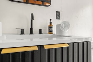 Ein Badezimmer mit einem weißen Waschbecken, einem schwarzen Wasserhahn und einer Handseifenflasche.
