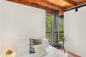 A bedroom with a bed, pillows, a lamp, and a view of the outdoors through a window.