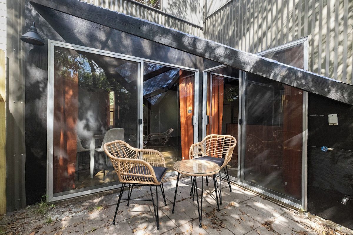 A patio with two wicker chairs and a small table, enclosed by glass doors and a wooden fence.