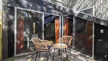 A patio with two wicker chairs and a small table, enclosed by glass doors and a wooden fence.