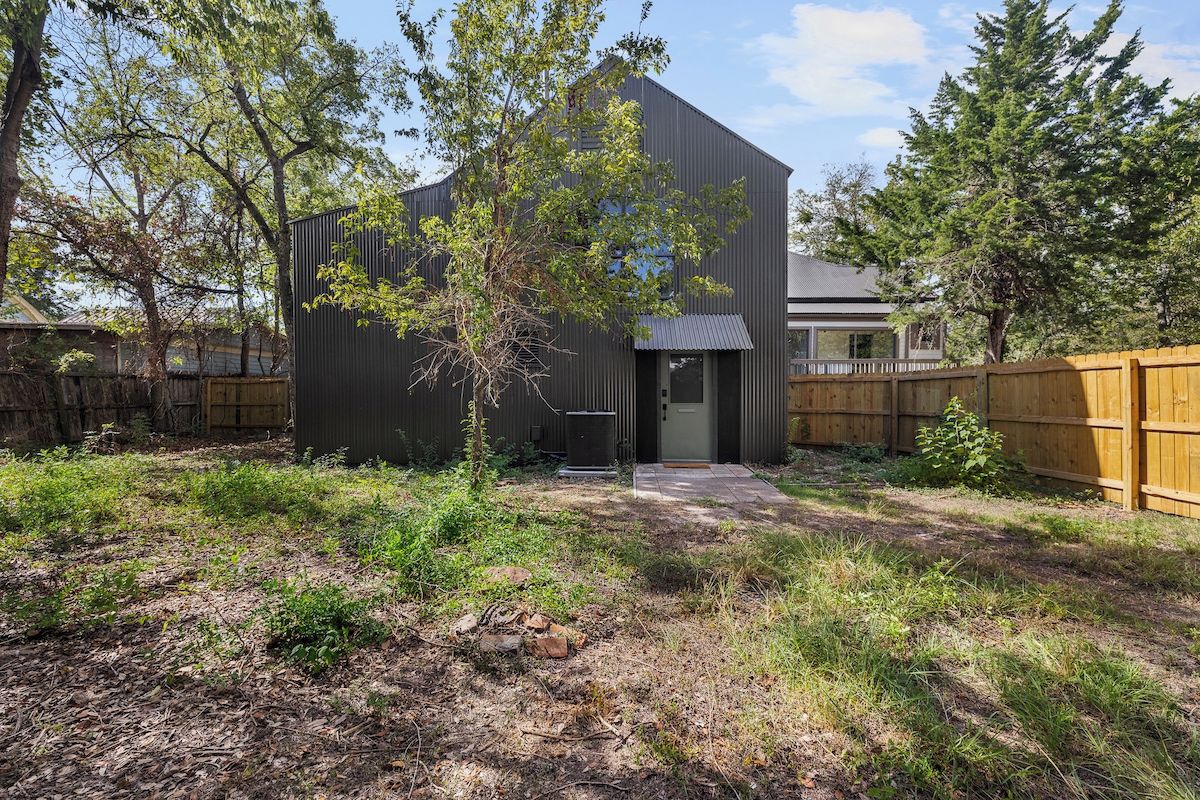 Un bâtiment moderne à l’extérieur sombre, doté d’une entrée bien visible et entouré d’une zone verdoyante avec des arbres.