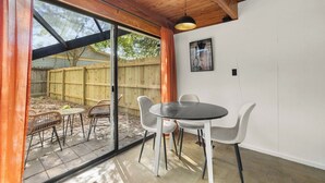 Une pièce dotée d’une grande porte-fenêtre coulissante donnant sur un patio extérieur, d’une table ronde avec des chaises et d’un unique luminaire suspendu.