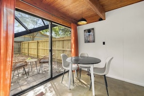 Ein Zimmer mit einer großen Schiebeglastür, die auf eine Terrasse im Freien führt, einem runden Tisch mit Stühlen und einer einzelnen Pendelleuchte.