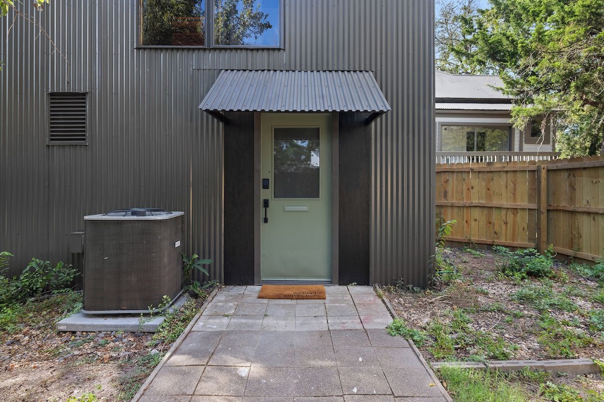 Un immeuble résidentiel avec une façade en métal, une porte verte et un petit espace porche.