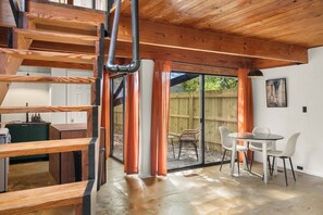 Un interior moderno con una escalera de madera, un comedor con sillas y vistas a un espacio exterior a través de puertas de cristal.