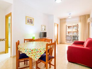 A living room with a red sofa, a dining table with chairs, a TV, and a window with curtains. - Oropesa Apartment With Terrace (Oropesa del Mar)