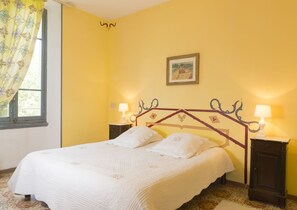 Ein Bett mit weißer Decke, zwei Nachttische mit Lampen, ein Fenster mit Vorhang und ein Bild an der Wand.
