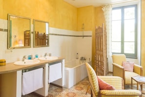 Ein Badezimmer mit zwei Waschbecken, einer Badewanne und einer Dusche. Zwei Stühle und ein Tisch sind ebenfalls vorhanden.