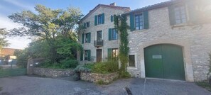 Ein Steinhaus mit grüner Tür und Fenstern, umgeben von viel Grün.