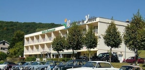 Ein Hotel mit mehreren Balkonen, einem Parkplatz und einer Bergkulisse.