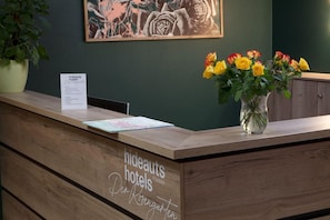 A reception desk with a wooden finish, a sign for 'hideauts hotels,' and a vase with yellow and orange flowers. - Villa Toscana (Fuessen)