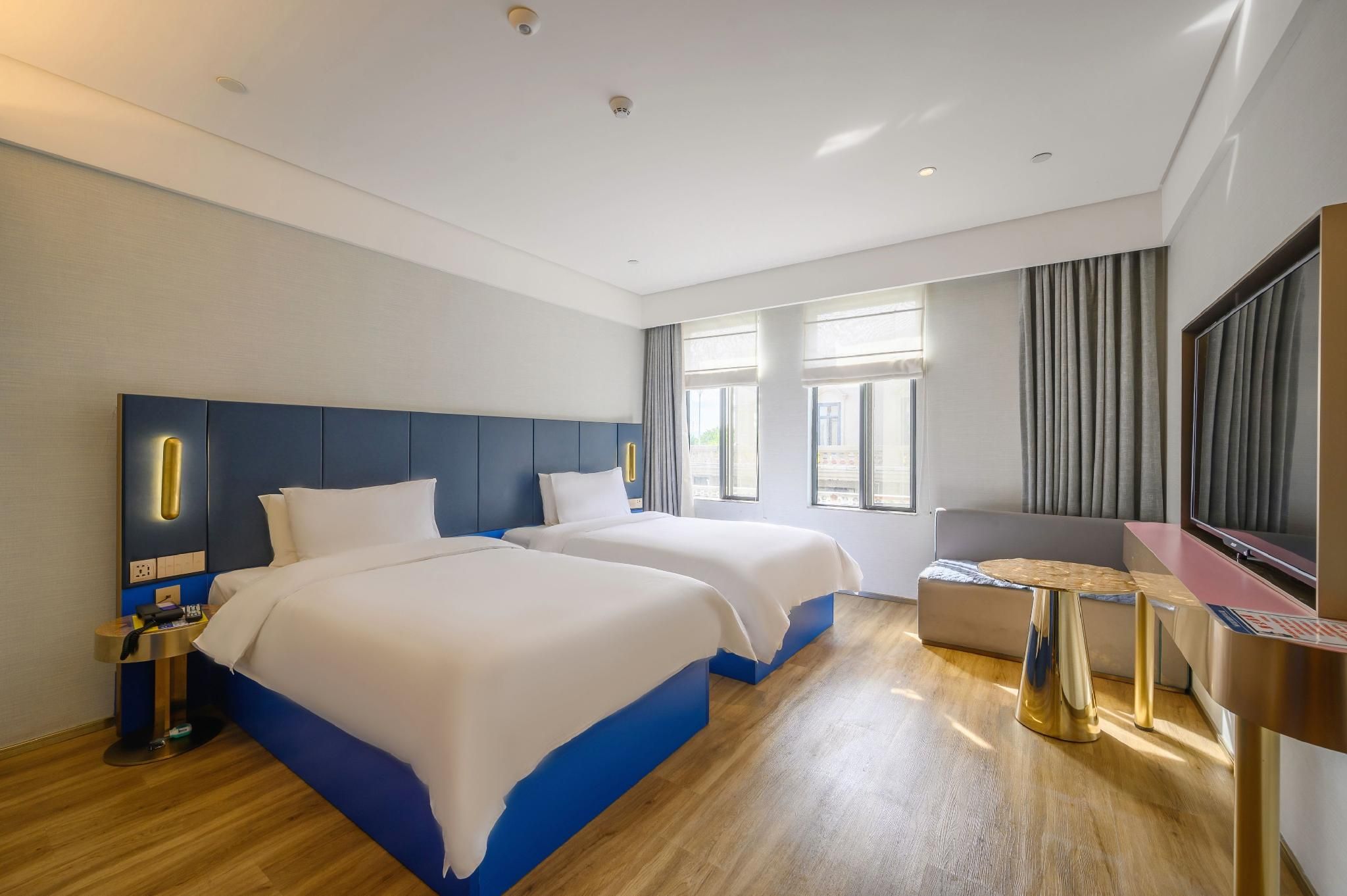 A hotel room with two beds, a desk, a TV, and a window with curtains.