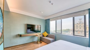 A hotel room with a bed, a TV mounted on the wall, a small table with a plant, and a window with a city view. - Spring Sunlight (Xiamen)