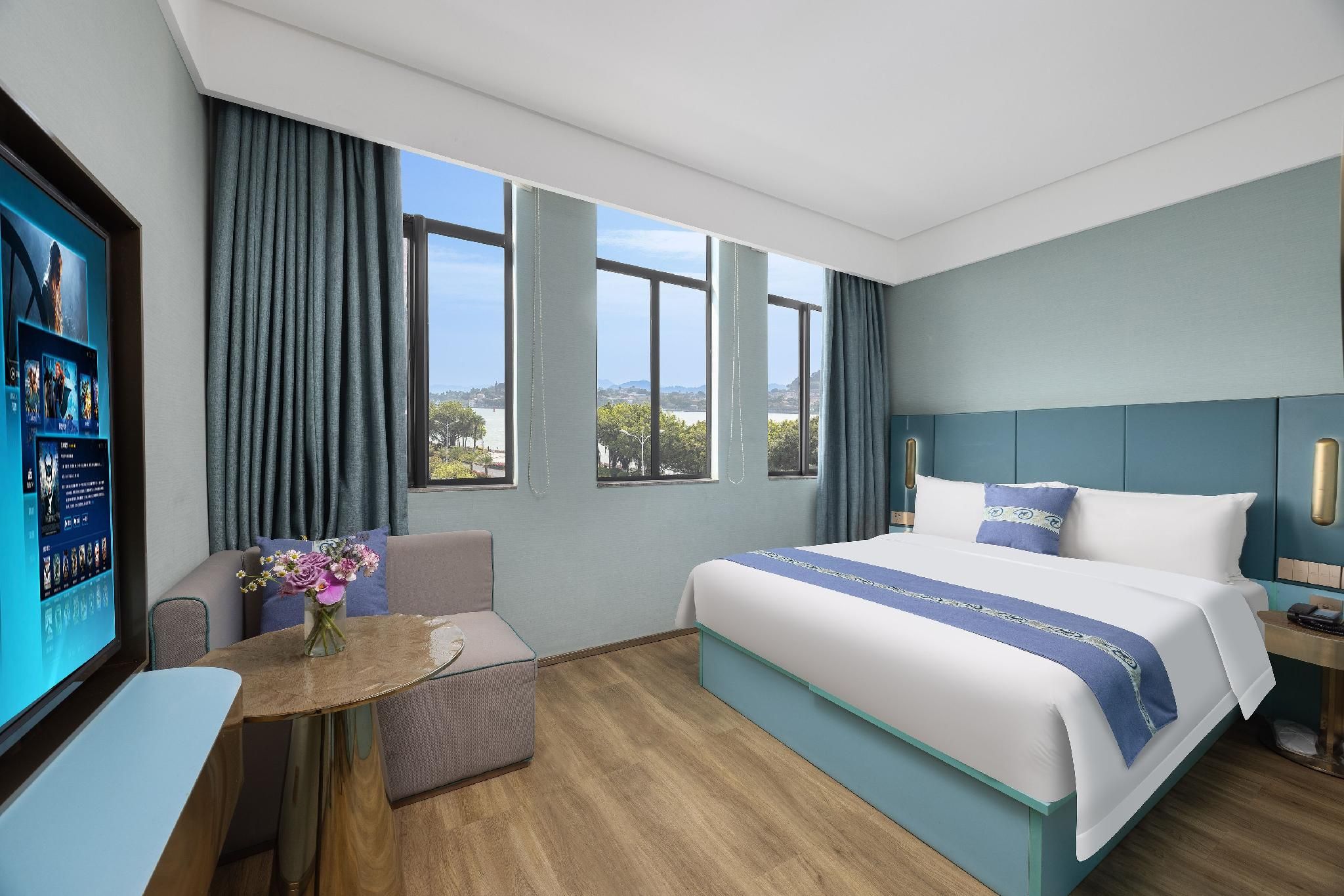 A hotel room with a large bed, a desk, a chair, a TV, and a view of the outdoors.