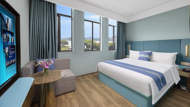 A hotel room with a large bed, a desk, a chair, a TV, and a view of the outdoors. - Spring Sunlight (Xiamen)