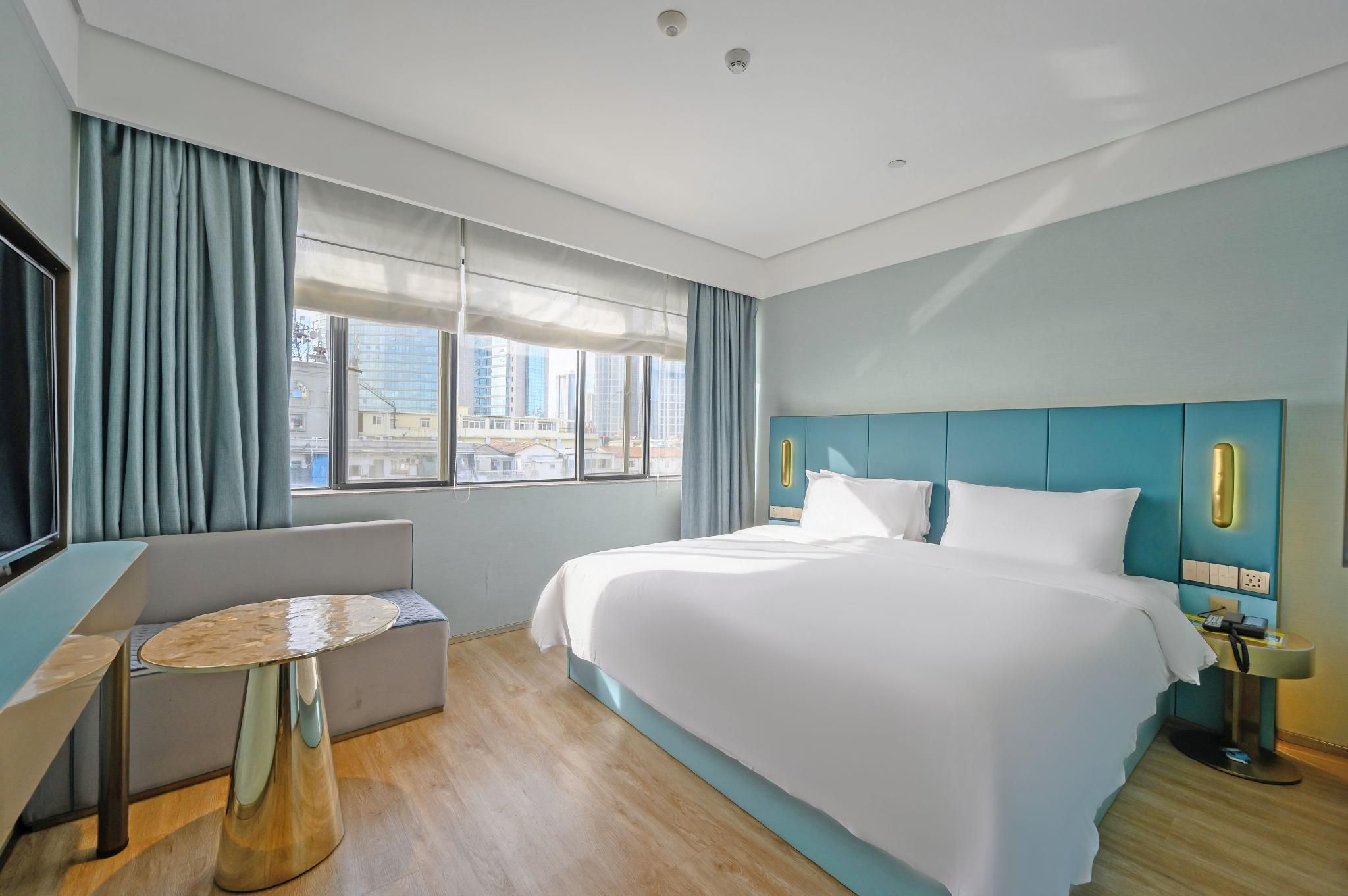 A hotel room with a large bed, a seating area, a desk, and a view of the cityscape.