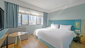 A hotel room with a large bed, a seating area, a desk, and a view of the cityscape. - Spring Sunlight (Xiamen)