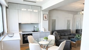 Uma cozinha moderna com armários brancos, uma mesa de jantar com cadeiras e um sofá cinza na sala de estar.