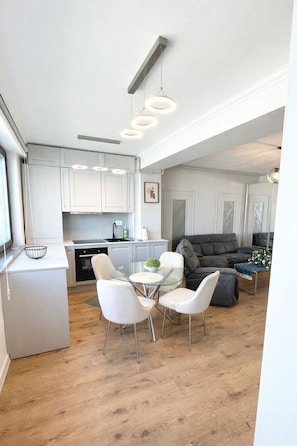A modern kitchen with white cabinets, a dining table with chairs, and a grey sofa in the living area. - Space Urbans  (Voluntari)