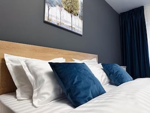 A hotel room with a wooden headboard, a bed with white and blue bedding, and a painting on the wall.