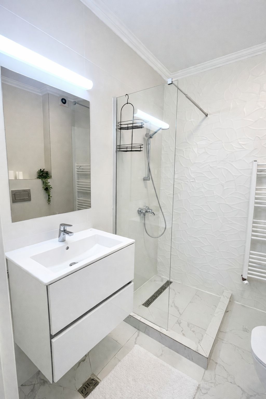 Un bagno moderno con cabina doccia in vetro, lavandino bianco e uno specchio grande.