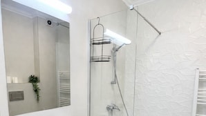 Casa de banho moderna com cabine de chuveiro em vidro, lavatório branco e espelho grande.