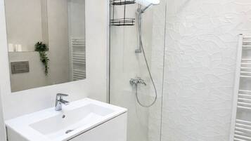 Un bagno moderno con cabina doccia in vetro, lavandino bianco e uno specchio grande.