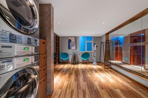 A commercial laundry room with stacked dryers and washing machines, a wooden floor, and a glass partition with a view. - Yitel (Guangzhou)