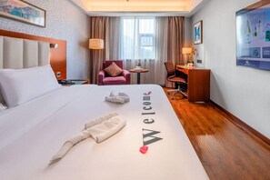 A hotel room with a bed, a desk, a chair, a TV, and a welcome mat. - Yitel (Guangzhou)