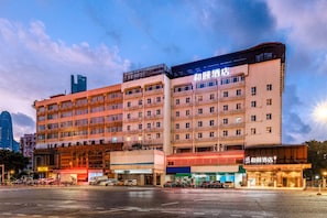 Un hotel de varios pisos con una fila de balcones, un restaurante a nivel de calle y un estacionamiento con coches.