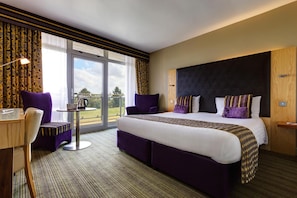 A hotel room with a large bed, a desk, a chair, and a view of the outdoors. - St Mellion International Resort (Saltash)