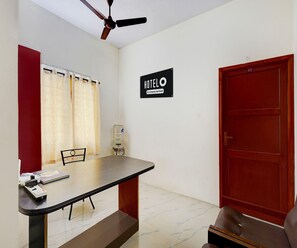 A hotel room with a single bed, a table with a chair, a water dispenser, and a ceiling fan. - Saver Double Ambience Home (Chennai)