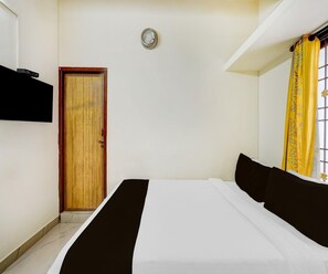 A room with a bed, a door, a wall-mounted TV, and a window with curtains. - Saver Double Ambience Home (Chennai)
