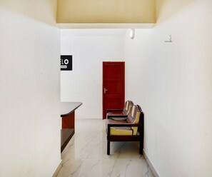 A hallway with a reception desk, a red door, and a bench with cushions. - Saver Double Ambience Home (Chennai)