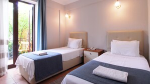 A hotel room with two beds, a small table, a chair, and a balcony with a view of greenery. - Villa Danlin Hotel (Fethiye)