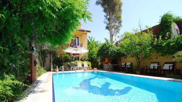 A swimming pool with lounge chairs and a pergola, surrounded by greenery and a building. - Villa Danlin Hotel (Fethiye)