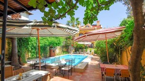 An outdoor pool area with tables and chairs, surrounded by greenery and a building in the background. - Villa Danlin Hotel (Fethiye)