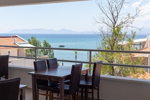 A balcony with a table and chairs, overlooking a body of water with a boat and mountains in the distance. - A.emreli Suite Hotel (Ayvalik)