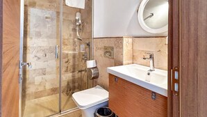 Un baño moderno con cabina de ducha de vidrio, inodoro, lavamanos con espejo y cubo de basura.