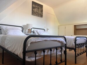A bedroom with two beds, a bedside lamp, and a cityscape painting on the wall. - Country house on the banks of the Eure River – Wooded grounds – Sleeps 10 (Cailly-sur-Eure)