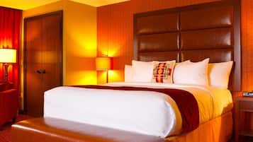 A hotel room with a large bed, a wooden headboard, a bench, a nightstand, and a lamp.