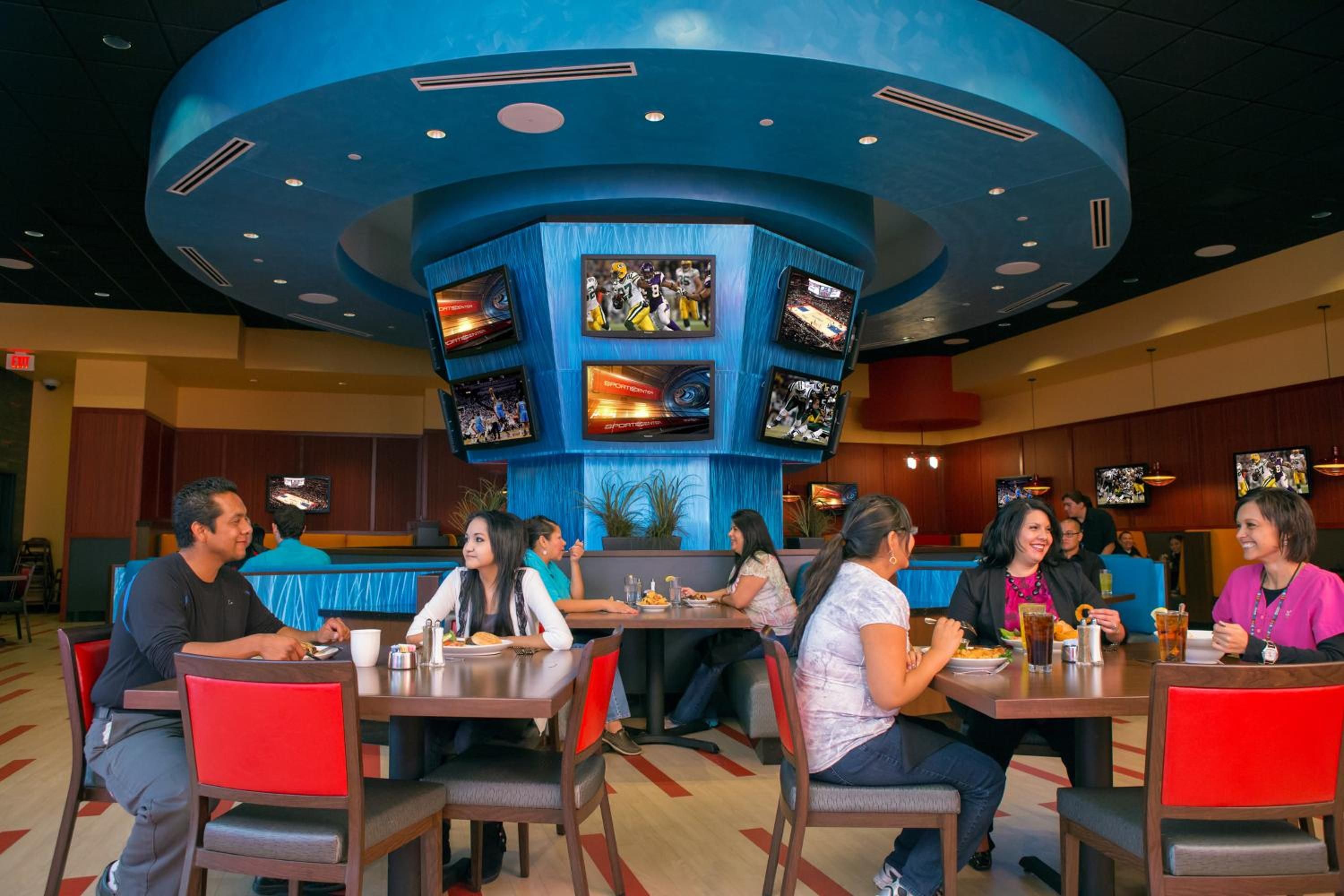 A restaurant with multiple screens displaying sports content, diners seated at tables, and a distinctive blue ceiling.