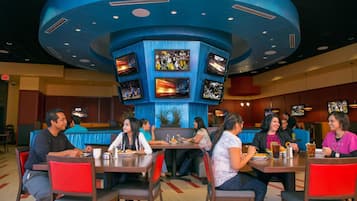 A restaurant with multiple screens displaying sports content, diners seated at tables, and a distinctive blue ceiling.