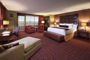 A hotel room with a large bed, a desk, a chair, a sofa, and a window with curtains.