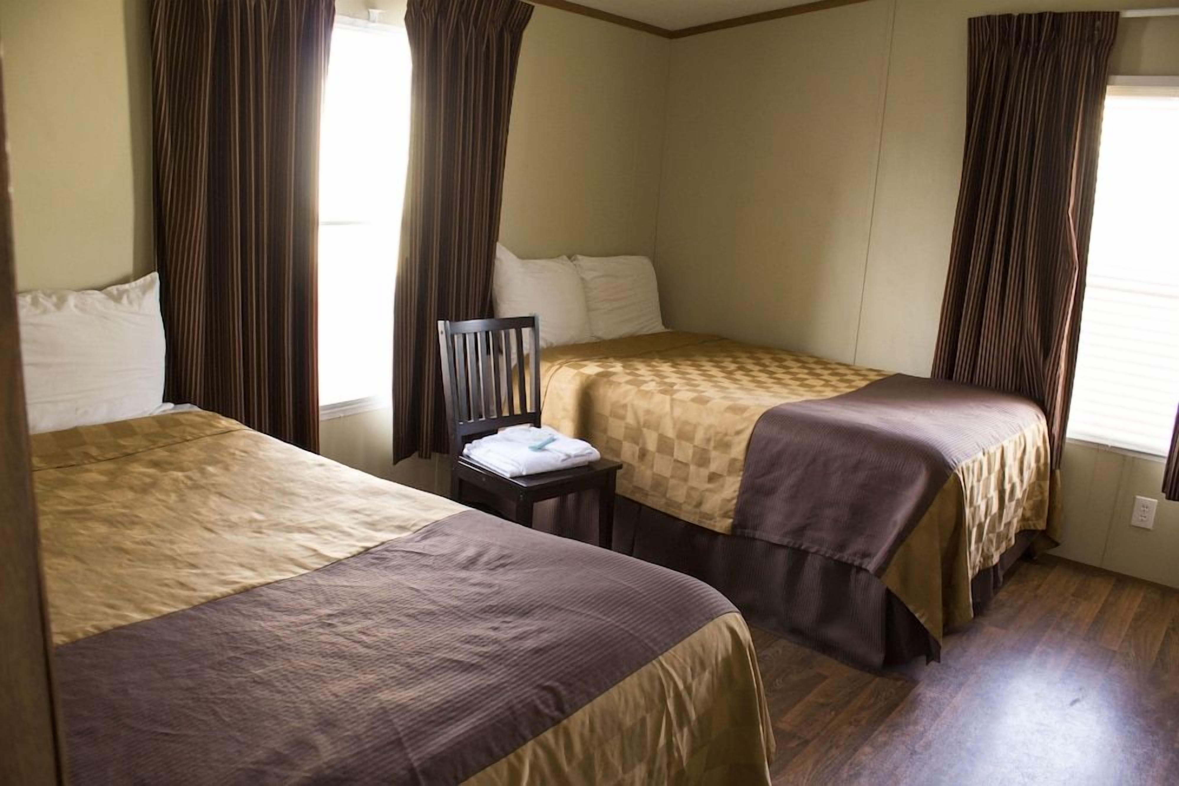 A hotel room with two beds, a nightstand, and curtains.