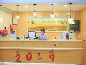A reception desk with a computer monitor, a telephone, and a framed landscape painting above. - 7 Days Inn Sea World 2nd Branch (Shenzhen)
